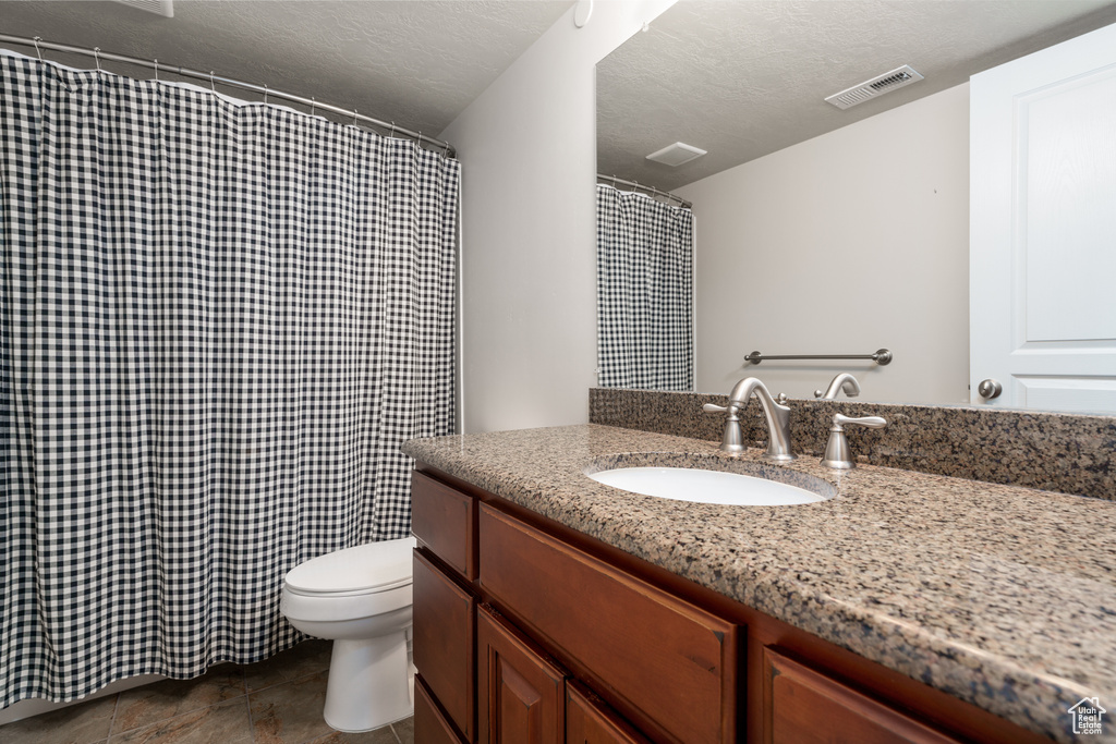 Bathroom with tile floors, toilet, a textured ceiling, and oversized vanity