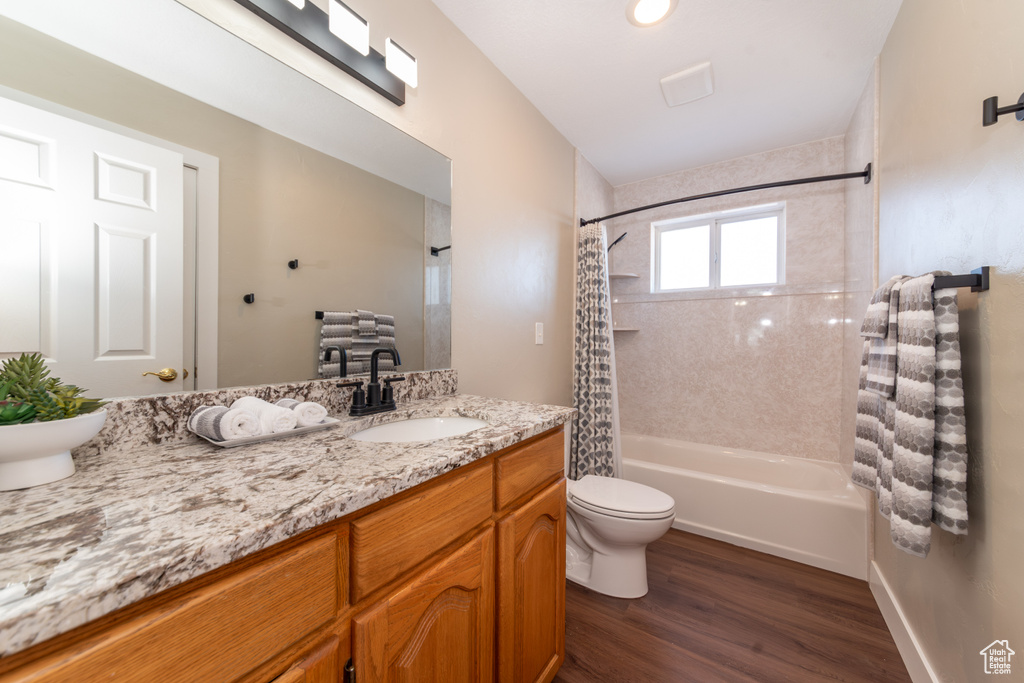 Full bathroom with shower / tub combo with curtain, hardwood / wood-style floors, large vanity, and toilet