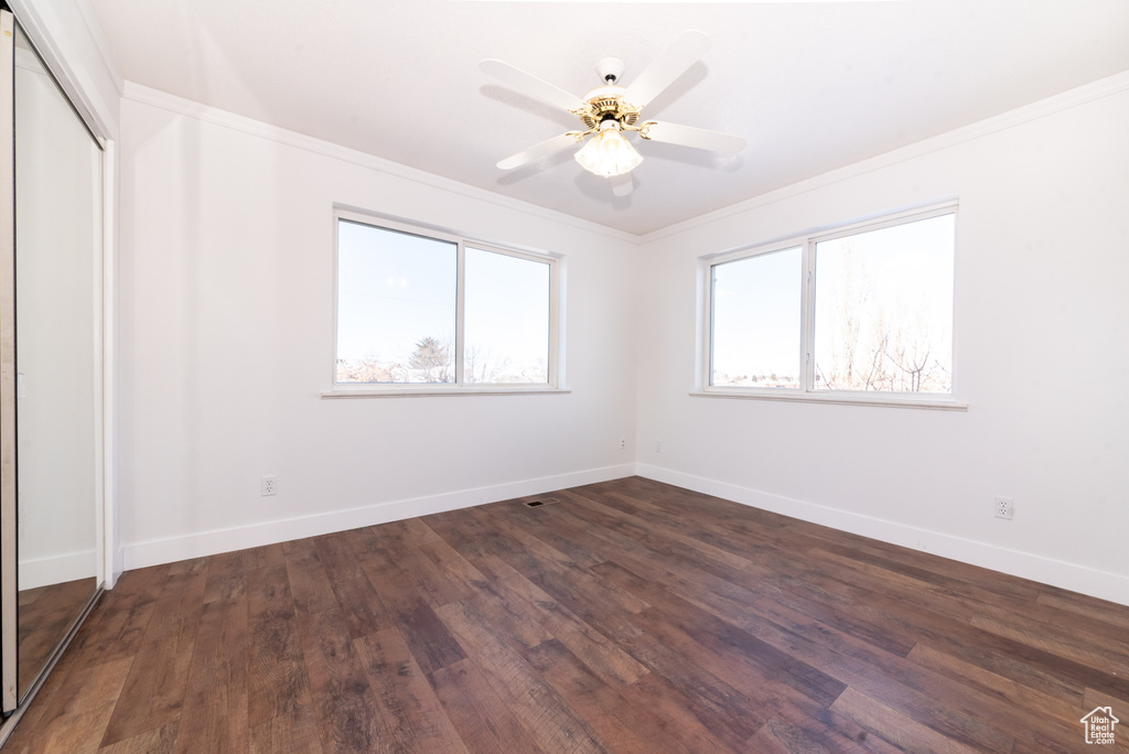 Empty room with dark hardwood / wood-style flooring, crown molding, and ceiling fan