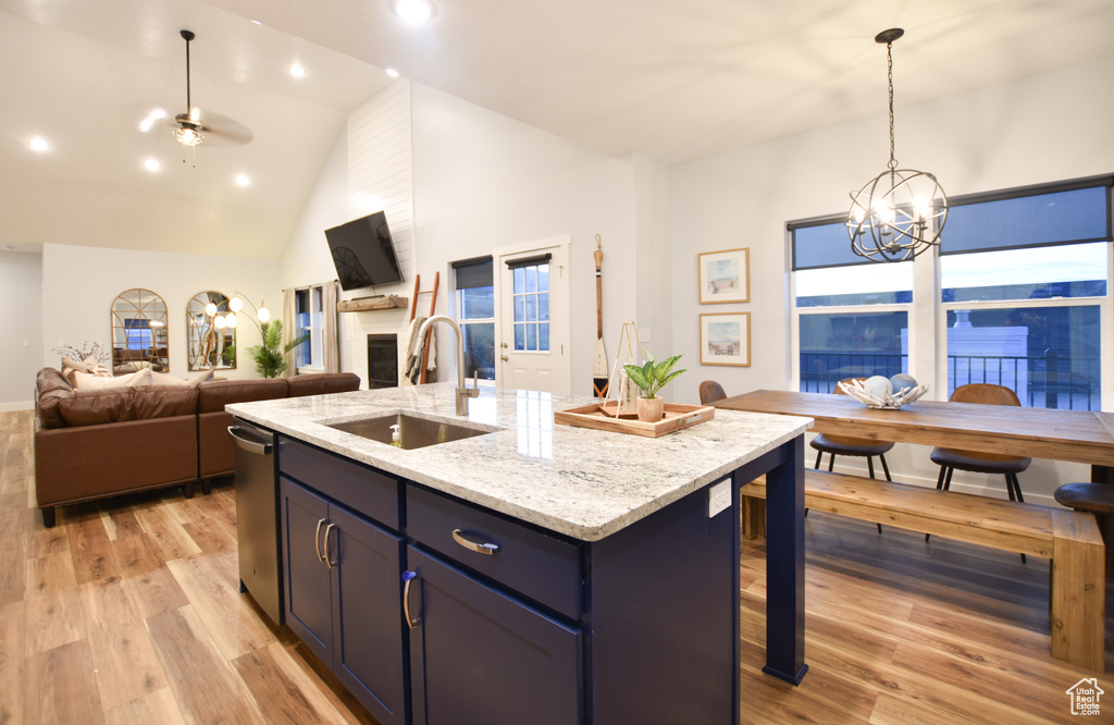 Kitchen featuring light wood-type flooring, light stone counters, ceiling fan with notable chandelier, decorative light fixtures, and a center island with sink