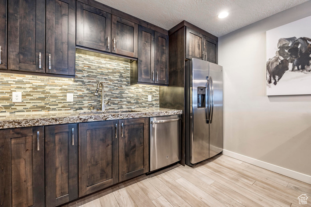 Kitchen featuring dark brown cabinets, light hardwood / wood-style floors, light stone countertops, and stainless steel appliances