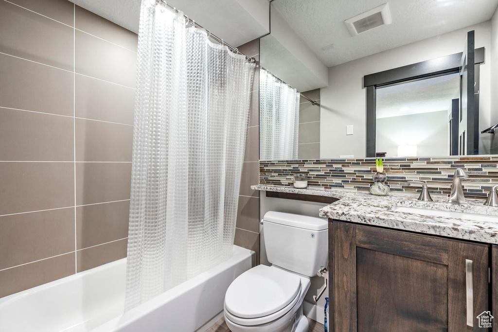 Full bathroom featuring tasteful backsplash, toilet, vanity, and shower / tub combo with curtain