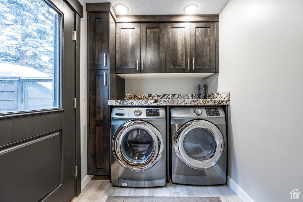 Clothes washing area with light hardwood / wood-style floors, washer and clothes dryer, and cabinets