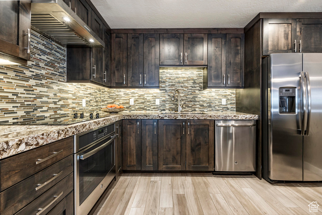 Kitchen with dark stone counters, light wood-type flooring, stainless steel appliances, and backsplash
