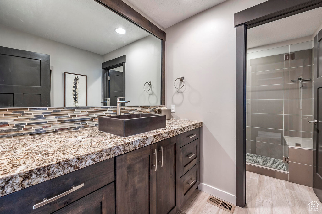 Bathroom with hardwood / wood-style floors, vanity, backsplash, and walk in shower