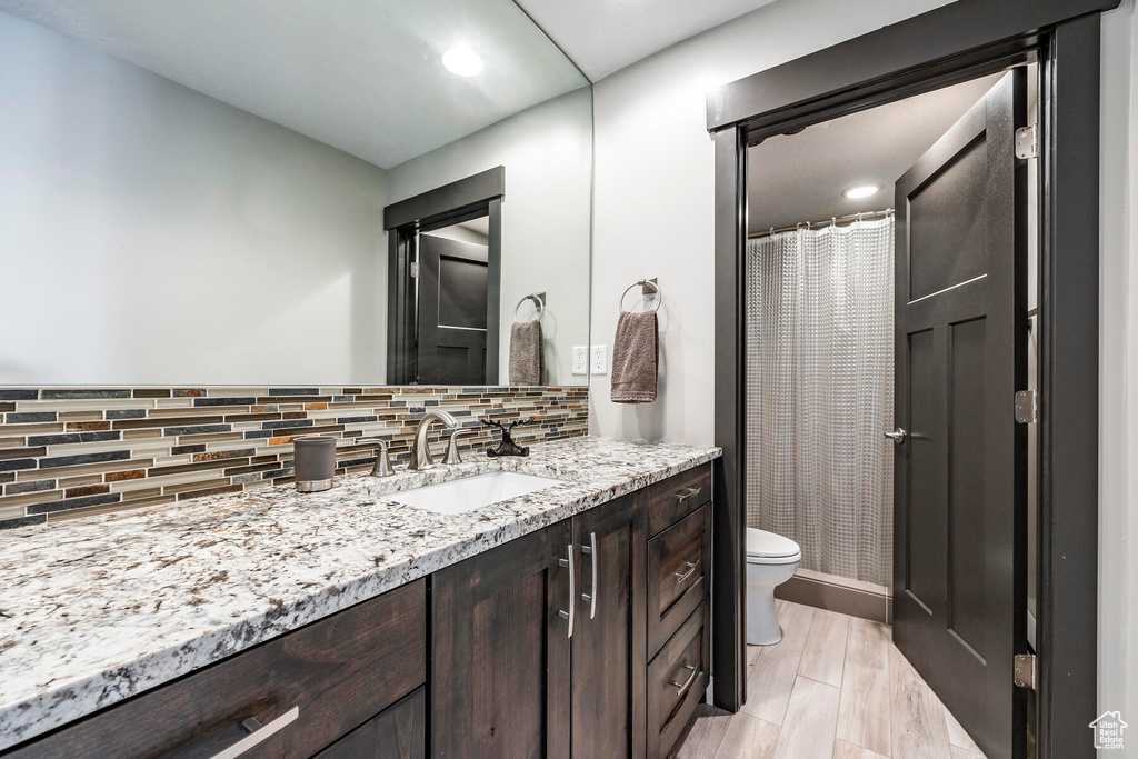 Bathroom featuring hardwood / wood-style floors, large vanity, toilet, and backsplash