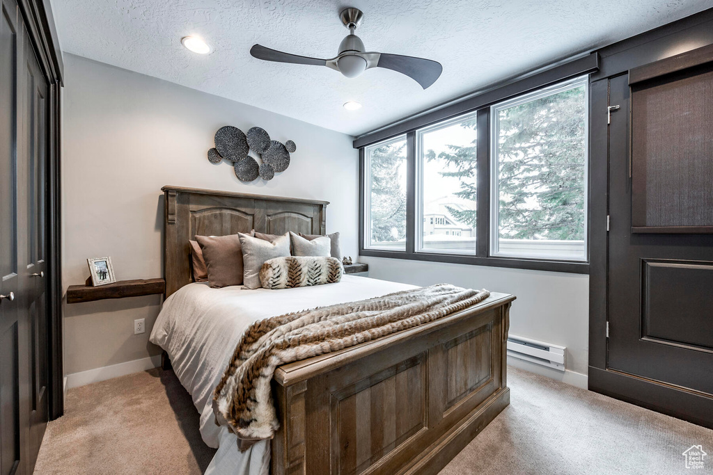 Bedroom featuring baseboard heating, light carpet, a textured ceiling, and ceiling fan