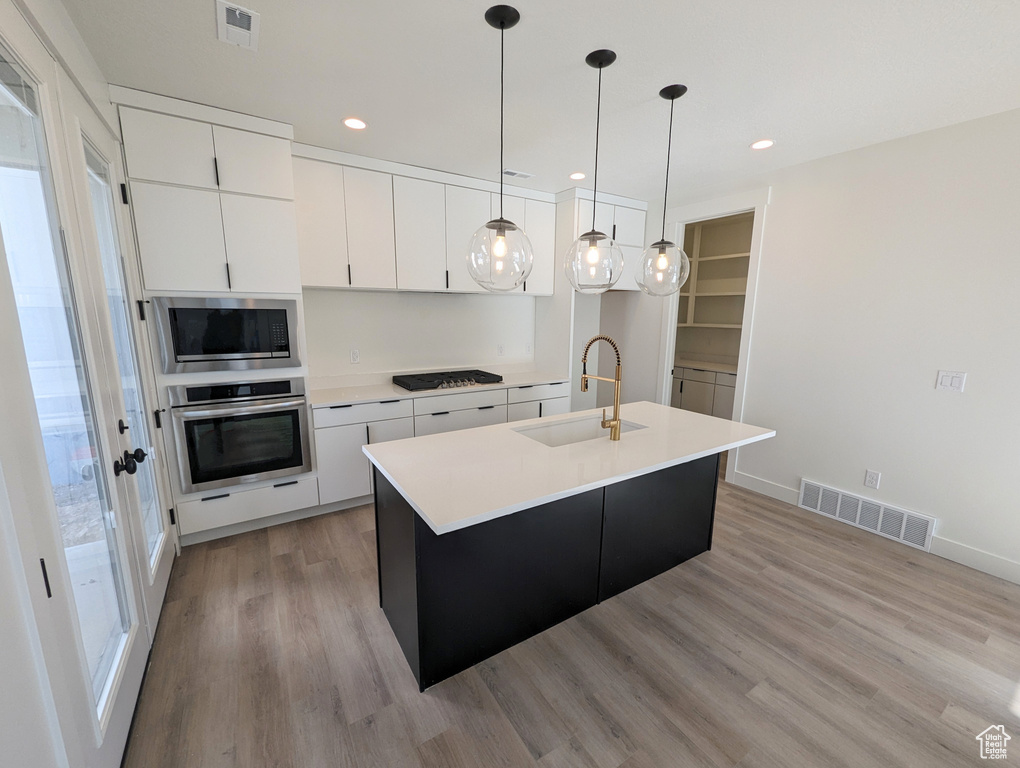 Kitchen with pendant lighting, appliances with stainless steel finishes, white cabinets, light wood-type flooring, and sink