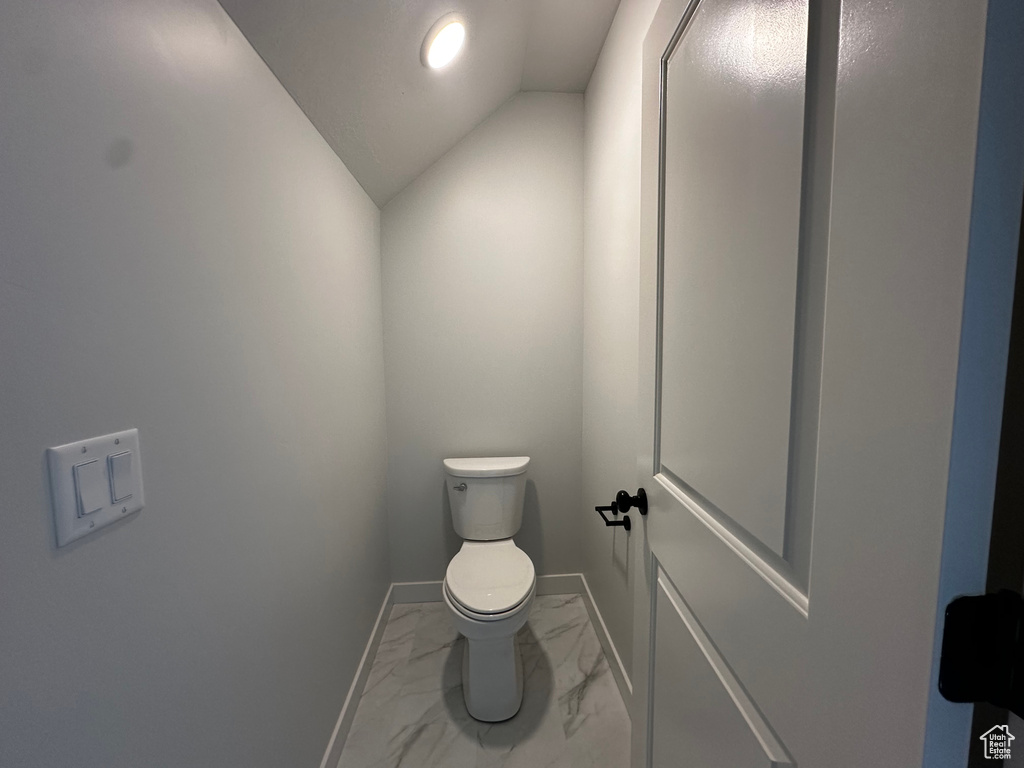 Bathroom with toilet, vaulted ceiling, and tile flooring