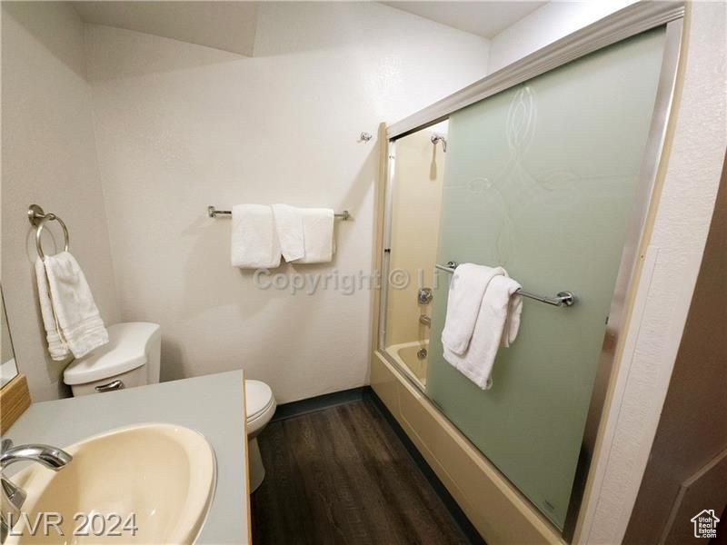 Full bathroom featuring wood-type flooring, sink, toilet, and bath / shower combo with glass door