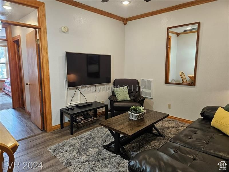 Living room with wood-type flooring, ornamental molding, and ceiling fan