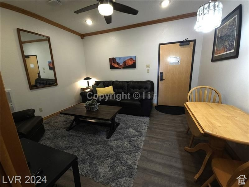 Living room featuring ornamental molding, dark wood-type flooring, and ceiling fan