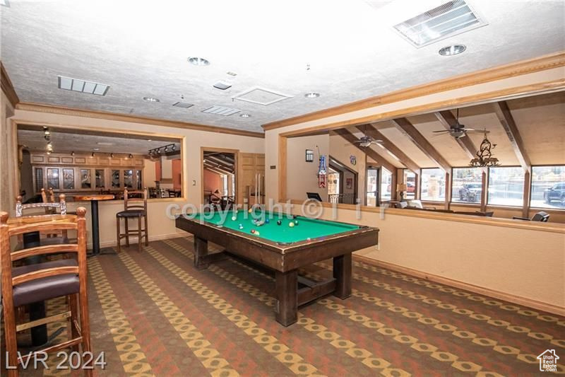 Playroom featuring dark carpet, ornamental molding, lofted ceiling with beams, ceiling fan, and billiards