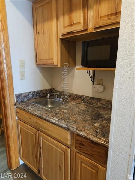Kitchen with sink, dark hardwood / wood-style floors, and dark stone countertops