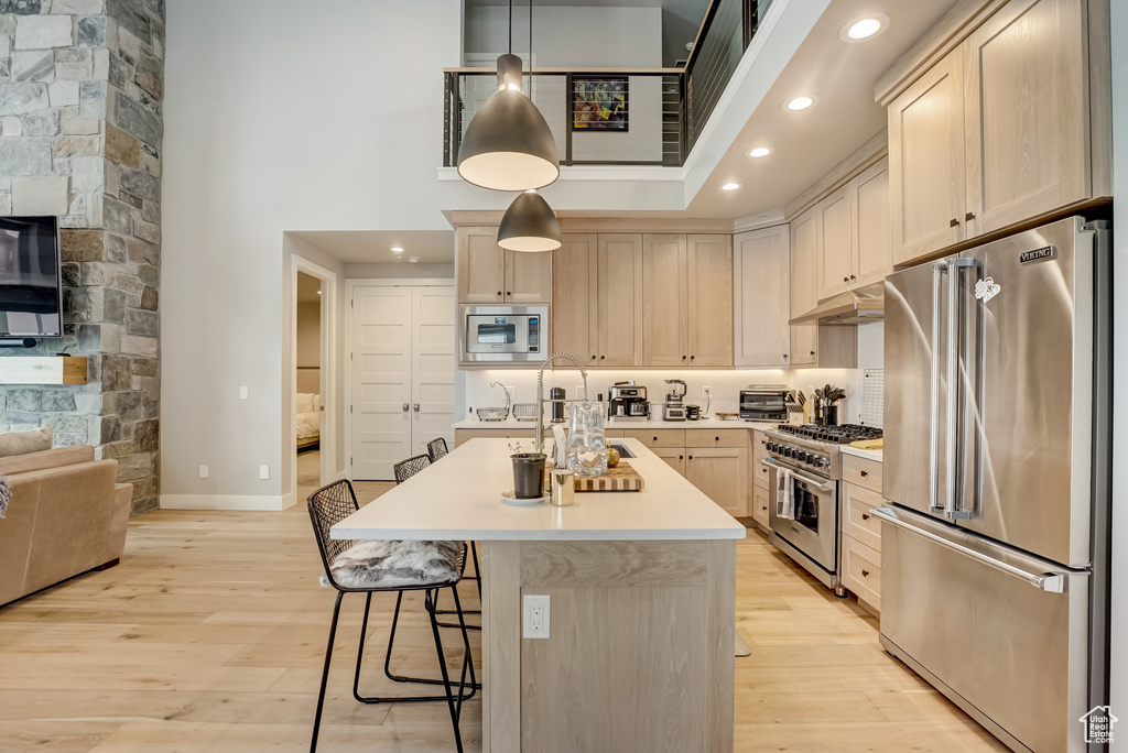 Kitchen featuring high quality appliances, a towering ceiling, light wood-type flooring, and hanging light fixtures