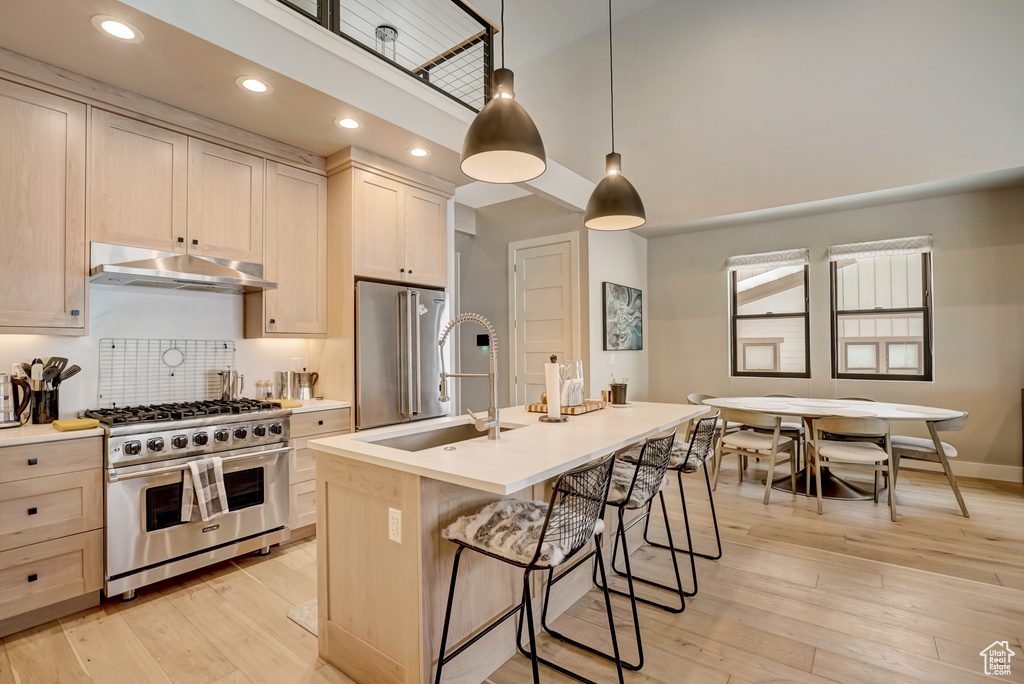 Kitchen with appliances with stainless steel finishes, decorative light fixtures, light hardwood / wood-style flooring, and a center island with sink