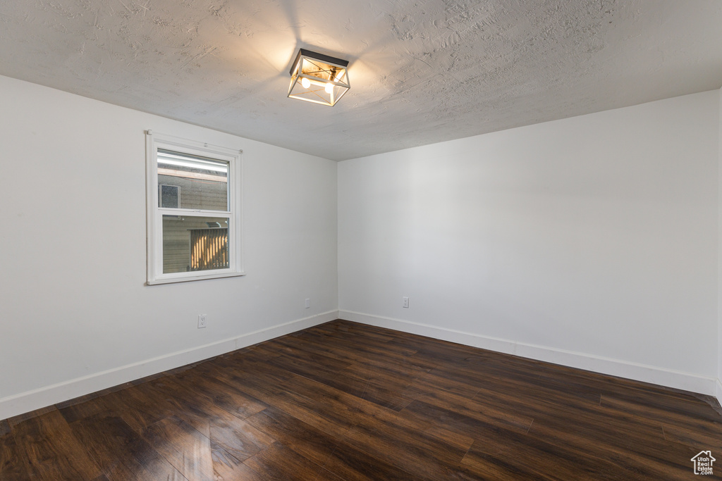 Empty room with dark hardwood / wood-style floors and a textured ceiling