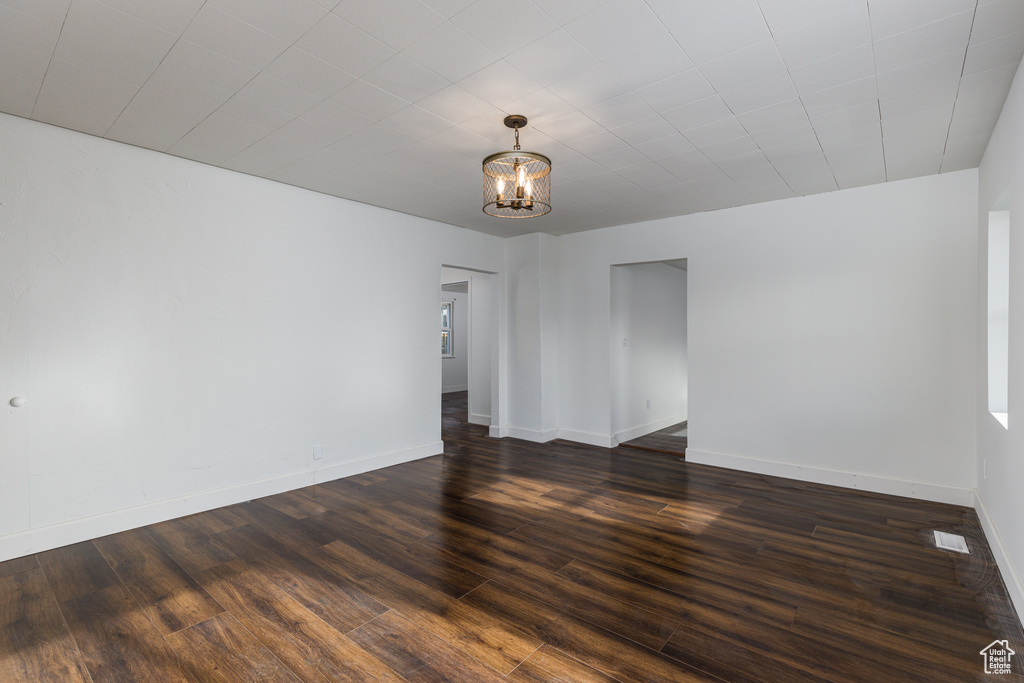 Unfurnished room with dark wood-type flooring and a chandelier