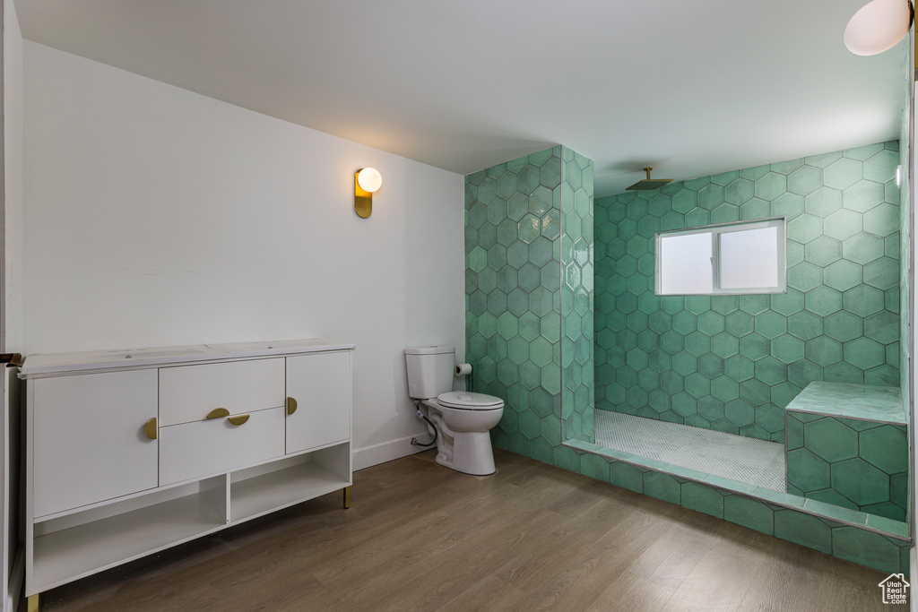 Bathroom with toilet, a tile shower, and hardwood / wood-style floors