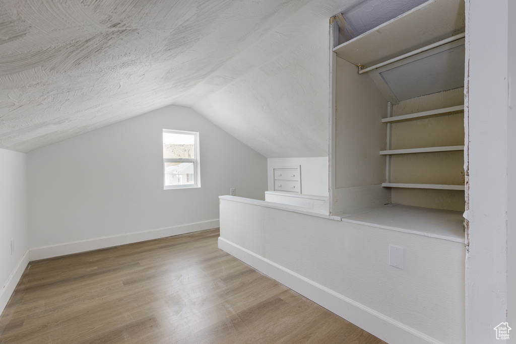 Additional living space featuring vaulted ceiling, a textured ceiling, and light hardwood / wood-style flooring