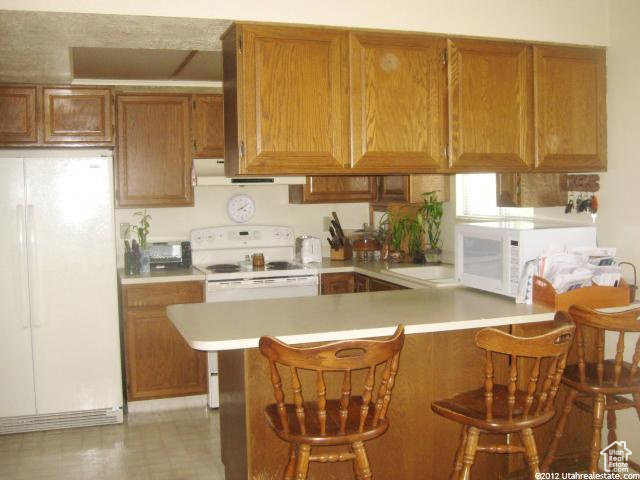 Kitchen featuring light tile flooring, kitchen peninsula, white appliances, and a kitchen breakfast bar