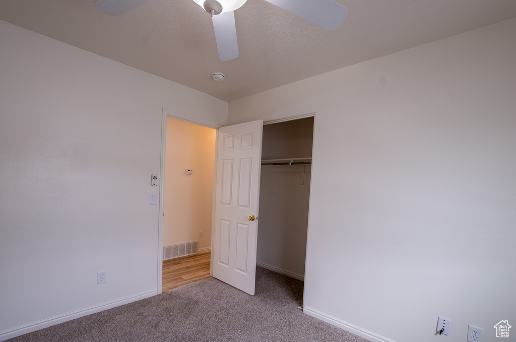 Unfurnished bedroom featuring a closet, light colored carpet, and ceiling fan