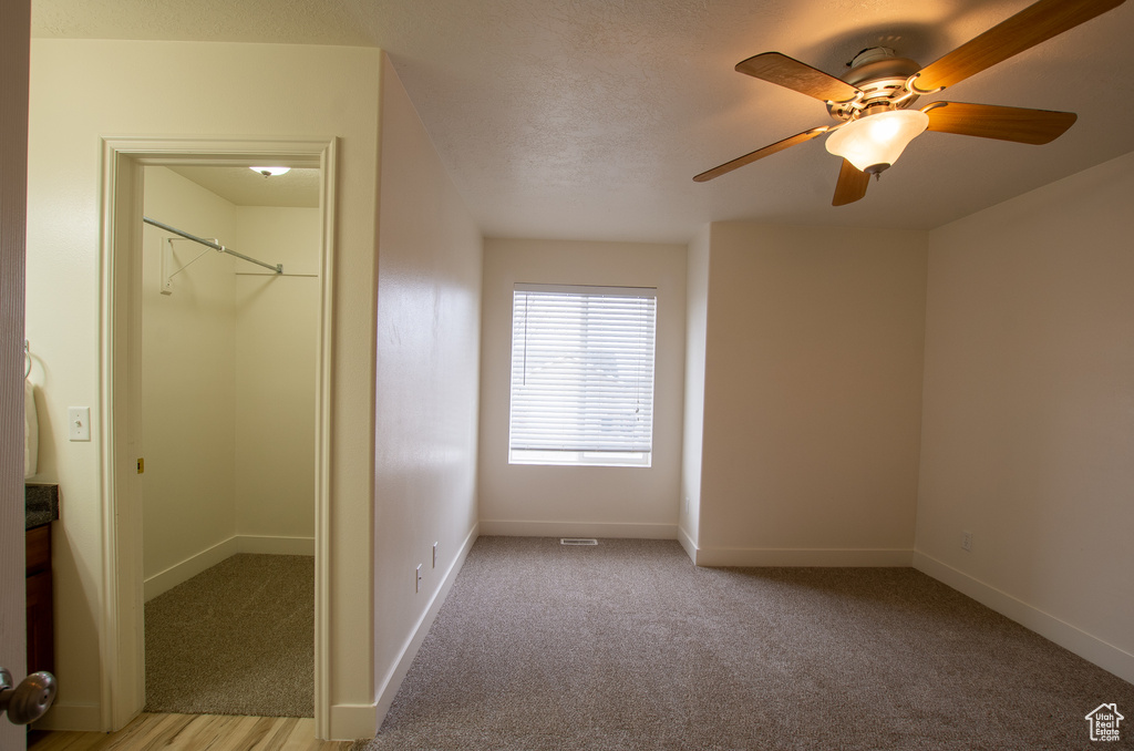 Unfurnished bedroom with light colored carpet, a closet, a walk in closet, and ceiling fan