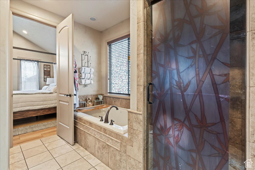 Bathroom with lofted ceiling, independent shower and bath, a wealth of natural light, and tile flooring