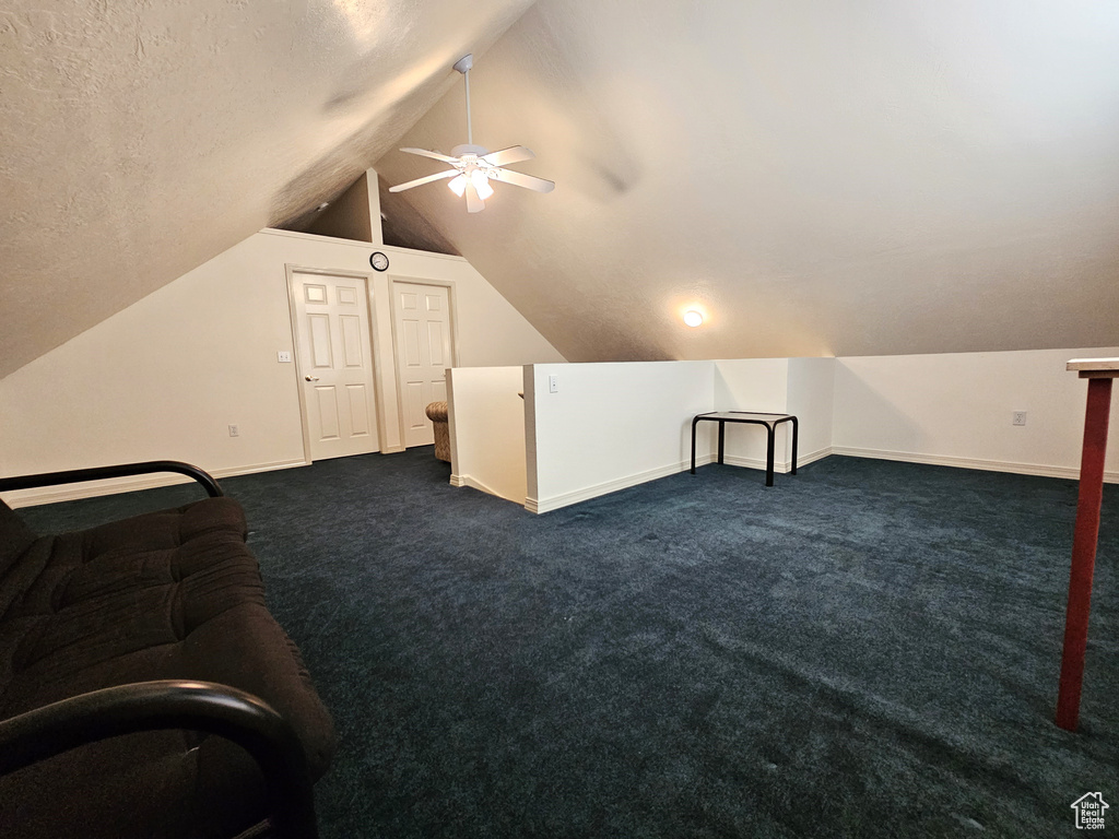 Additional living space featuring dark carpet, a textured ceiling, lofted ceiling, and ceiling fan