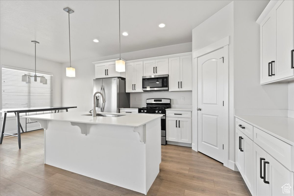Kitchen with hanging light fixtures, a center island with sink, appliances with stainless steel finishes, and white cabinetry