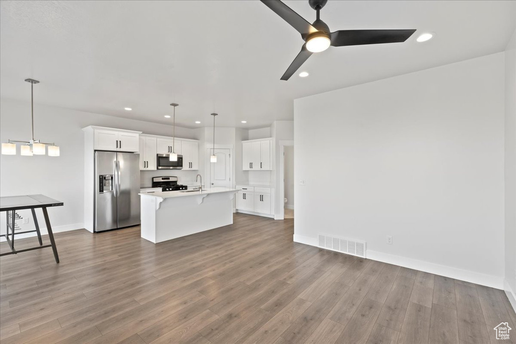Kitchen featuring white cabinets, appliances with stainless steel finishes, pendant lighting, wood-type flooring, and ceiling fan