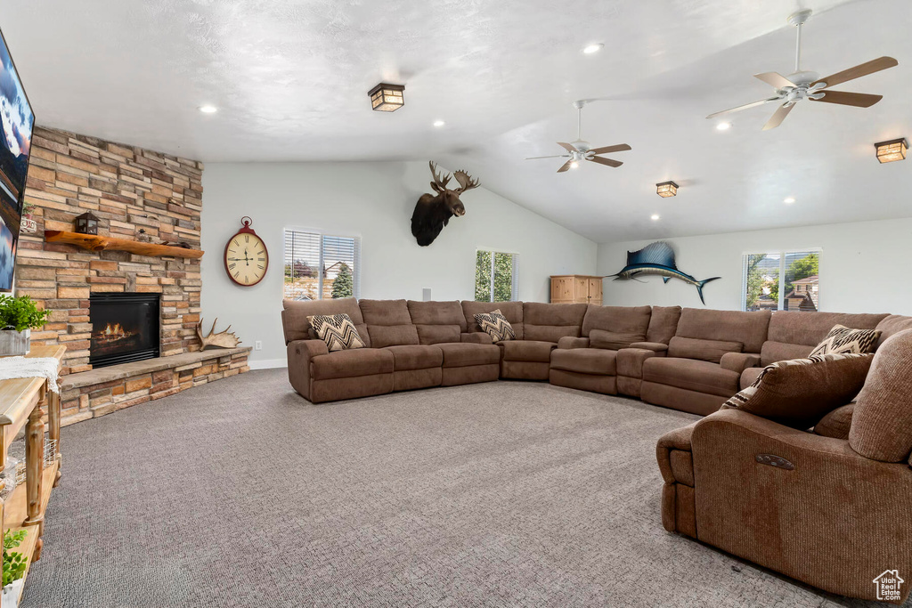 Carpeted living room featuring lofted ceiling, ceiling fan, and a stone fireplace