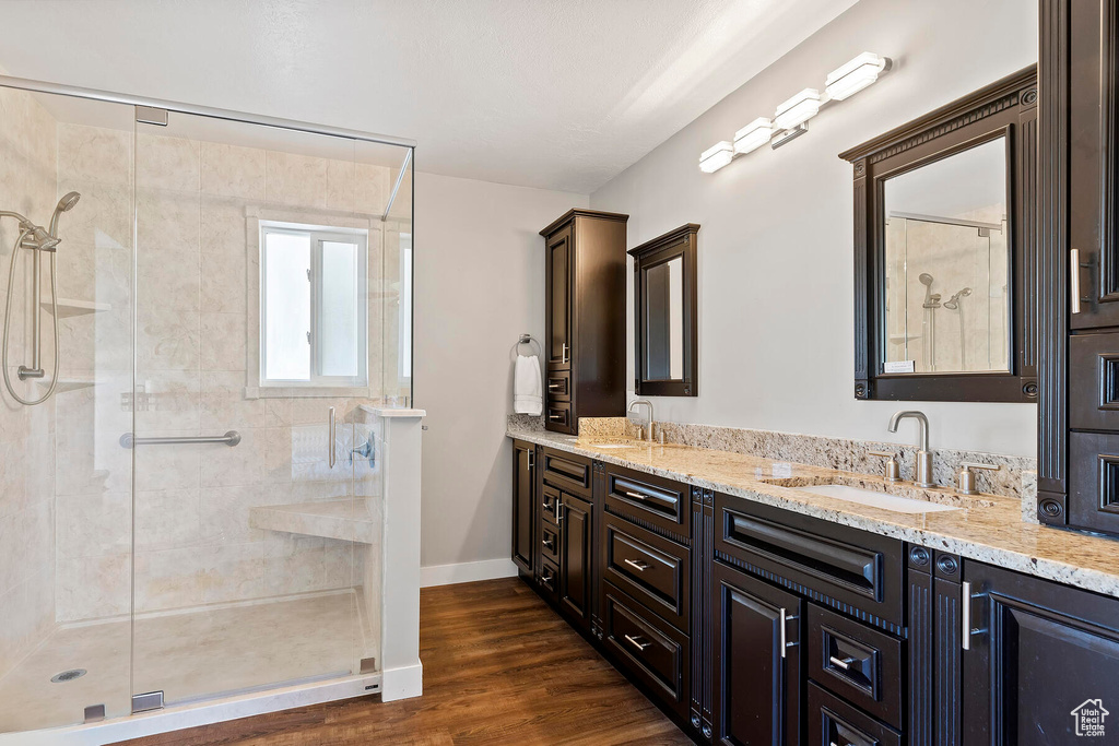 Bathroom with walk in shower, vanity with extensive cabinet space, hardwood / wood-style flooring, and dual sinks