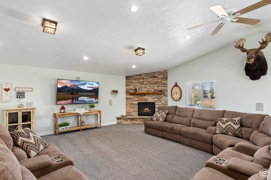 Living room featuring ceiling fan, a fireplace, vaulted ceiling, and carpet flooring
