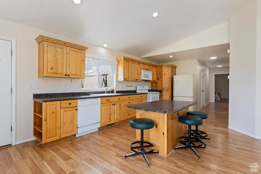 Kitchen featuring light hardwood / wood-style floors, white appliances, a breakfast bar area, and lofted ceiling