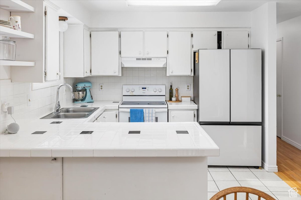 Kitchen featuring tile countertops, sink, white appliances, and kitchen peninsula