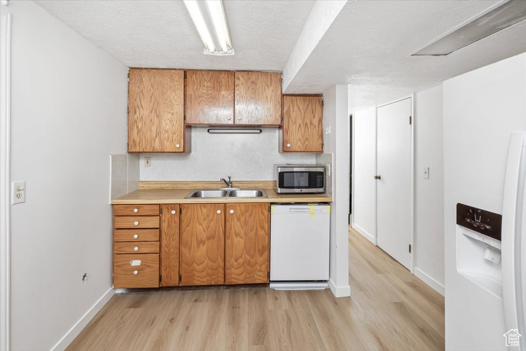 Kitchen featuring sink, dishwasher, light hardwood / wood-style floors, and a textured ceiling