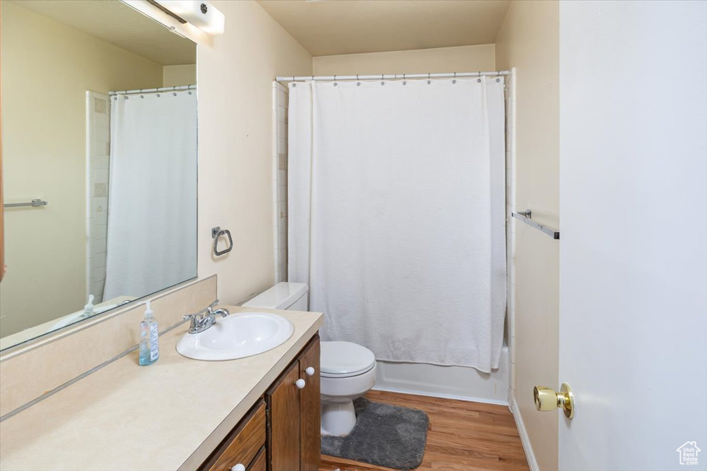 Full bathroom with wood-type flooring, vanity, toilet, and shower / bathtub combination with curtain