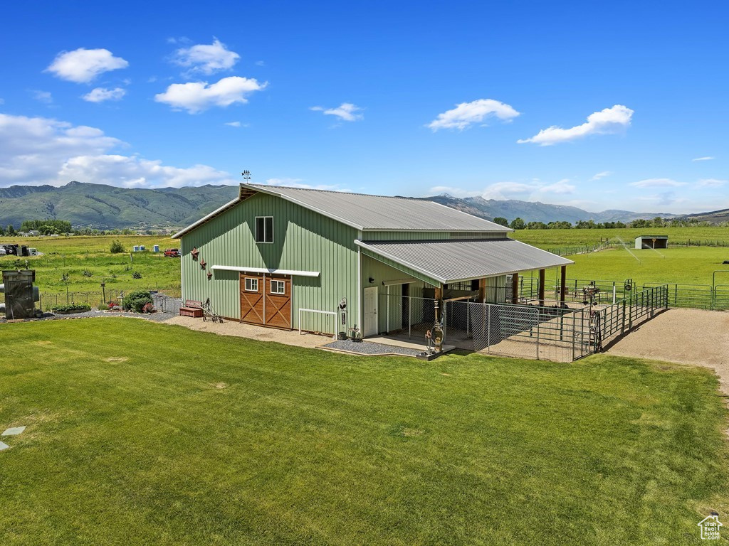 Back of house with an outdoor structure, a rural view, a lawn, and a mountain view