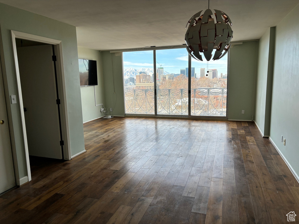 Empty room featuring dark wood-type flooring, a chandelier, and a healthy amount of sunlight