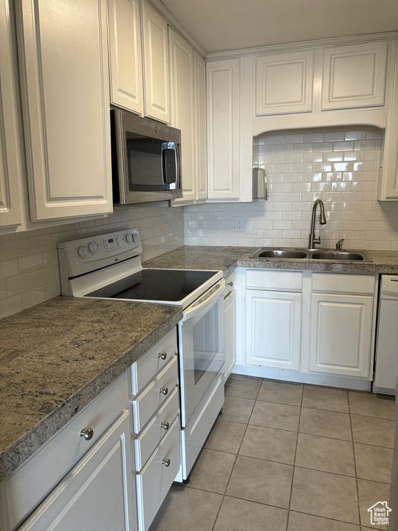 Kitchen featuring white electric range oven, white cabinetry, sink, and backsplash