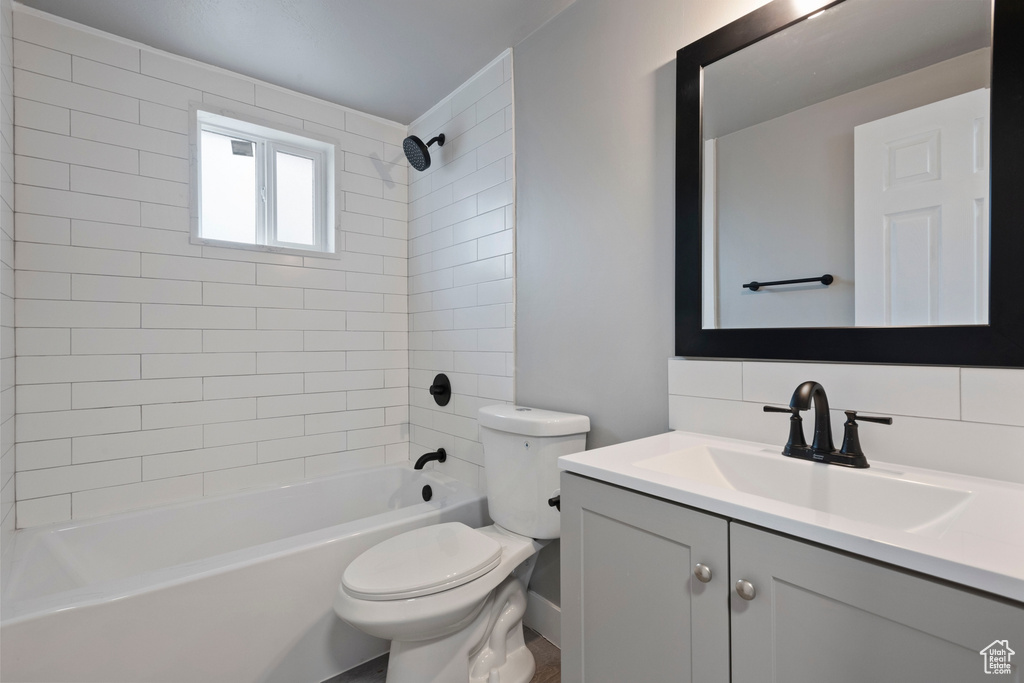 Full bathroom featuring toilet, vanity, tiled shower / bath combo, and backsplash