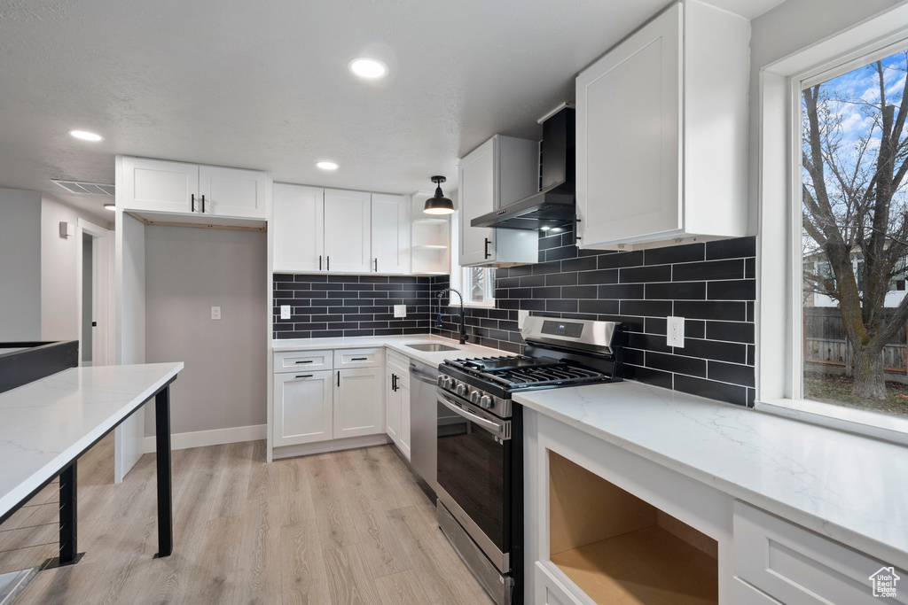 Kitchen with light hardwood / wood-style floors, wall chimney exhaust hood, stainless steel gas range, backsplash, and dishwashing machine