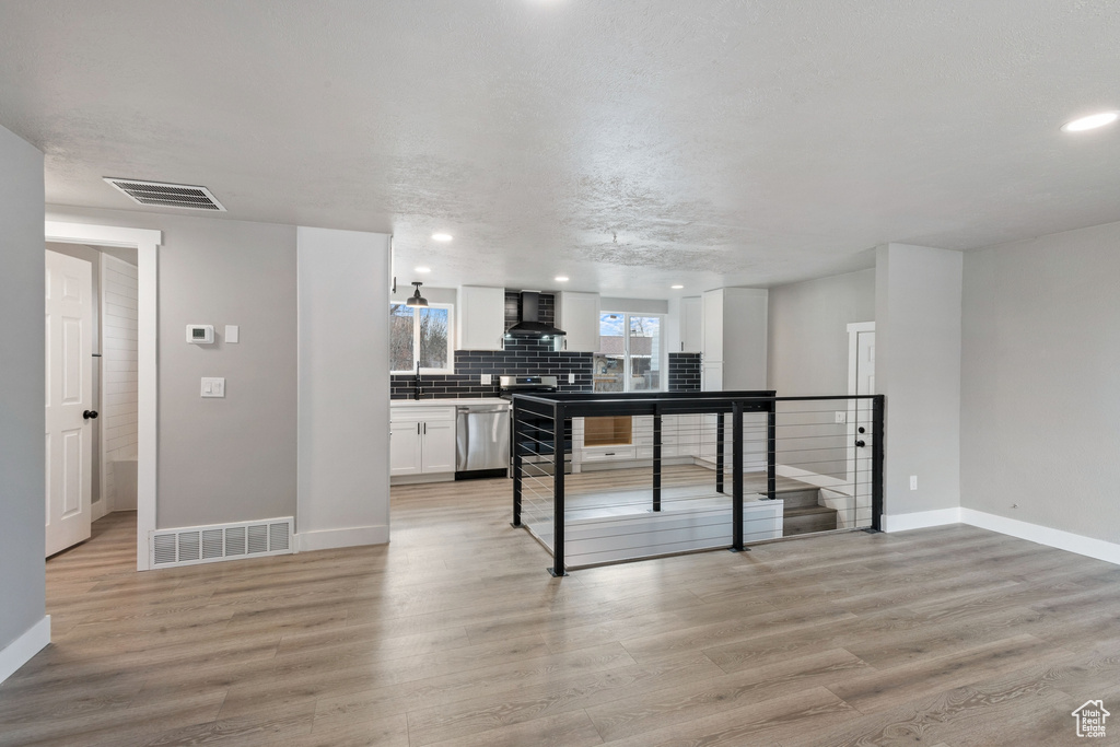 Kitchen with light hardwood / wood-style floors, wall chimney exhaust hood, white cabinetry, backsplash, and dishwasher