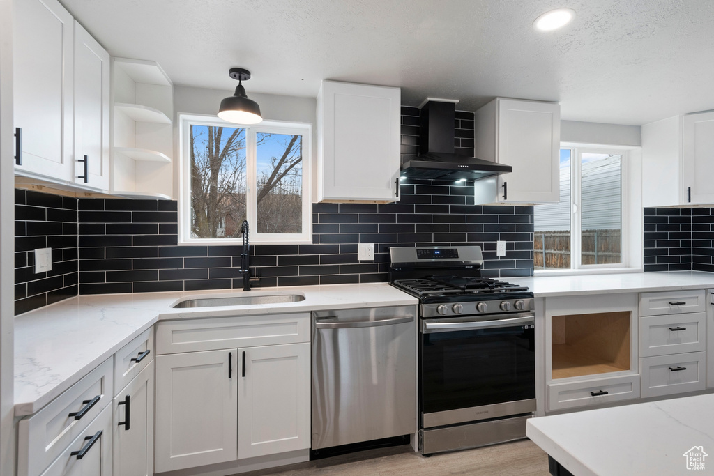 Kitchen with sink, stainless steel appliances, wall chimney range hood, and white cabinetry