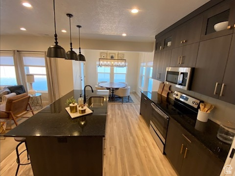 Kitchen featuring appliances with stainless steel finishes, an island with sink, a kitchen breakfast bar, and light wood-type flooring