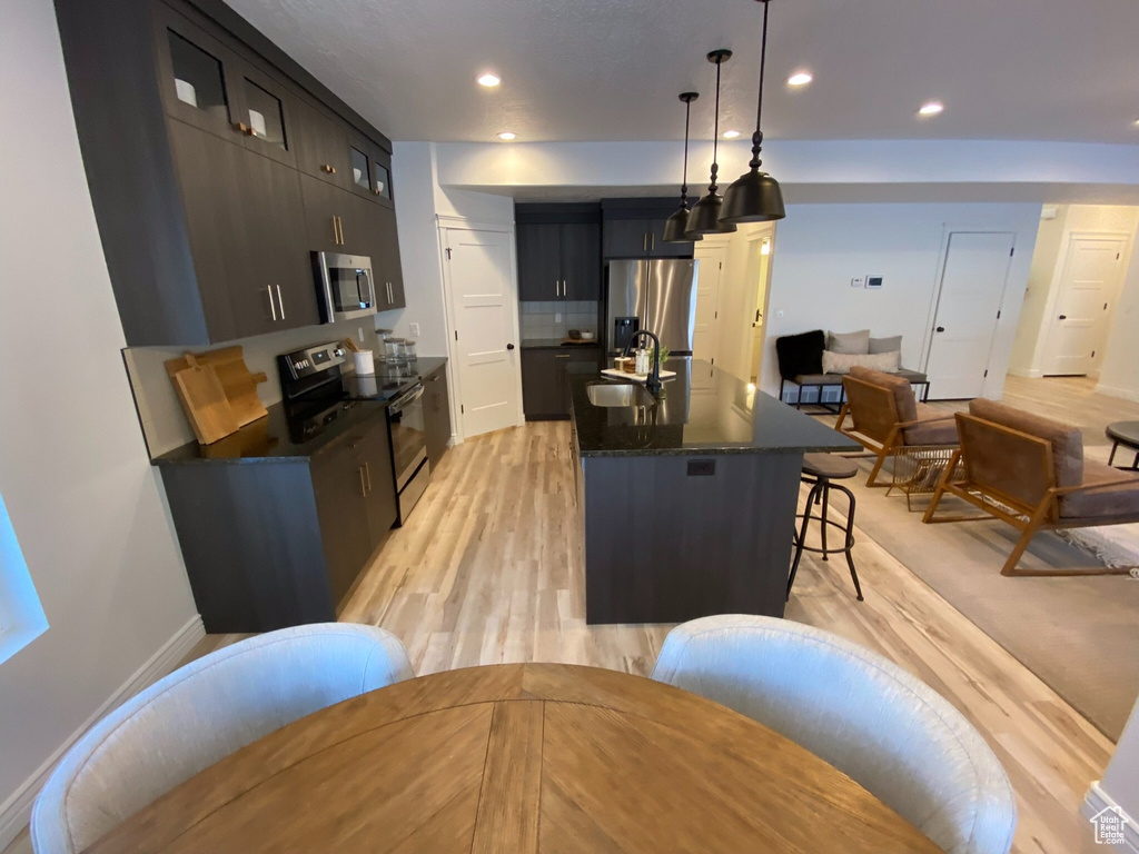Kitchen featuring stainless steel appliances, a breakfast bar, a center island with sink, sink, and decorative light fixtures