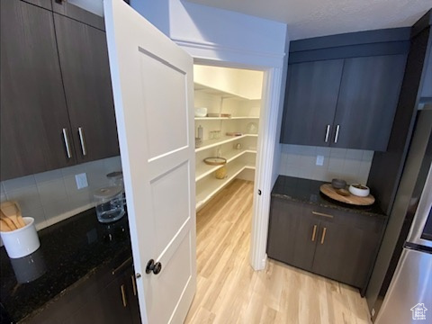 Kitchen featuring tasteful backsplash, dark brown cabinetry, light wood-type flooring, and dark stone countertops