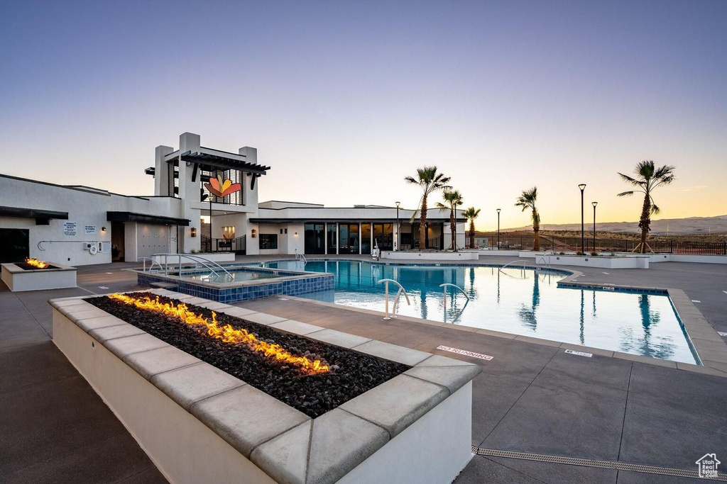 Pool at dusk featuring a fire pit, a community hot tub, and a patio