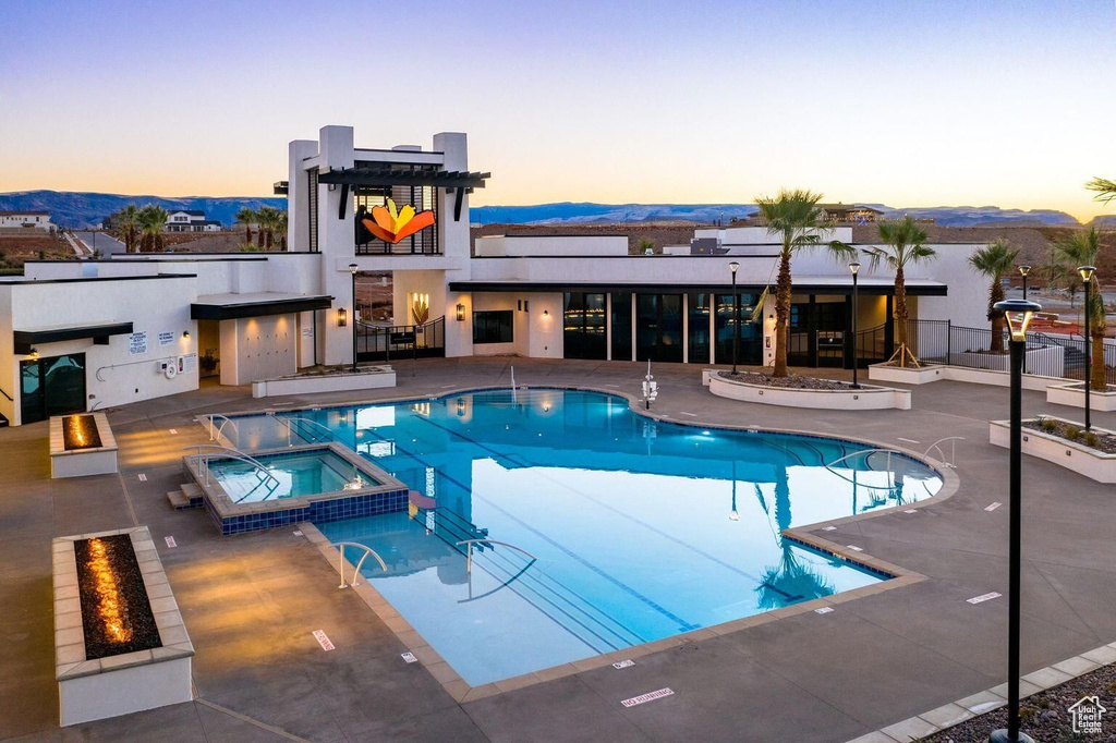 Pool at dusk with an outdoor fire pit, a hot tub, and a patio